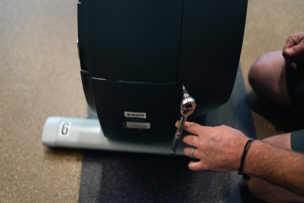 A technician using a wrench on a piece of gym equipment.